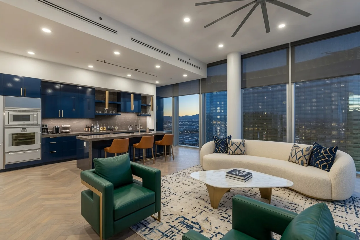 Dark roller shades frame city views in a living room with a white sofa and blue kitchen