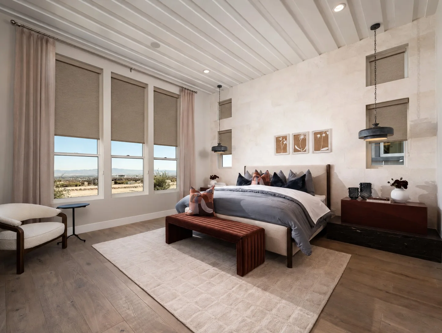 Soft neutral roller shades along tall bedroom windows beneath white ceiling beams
